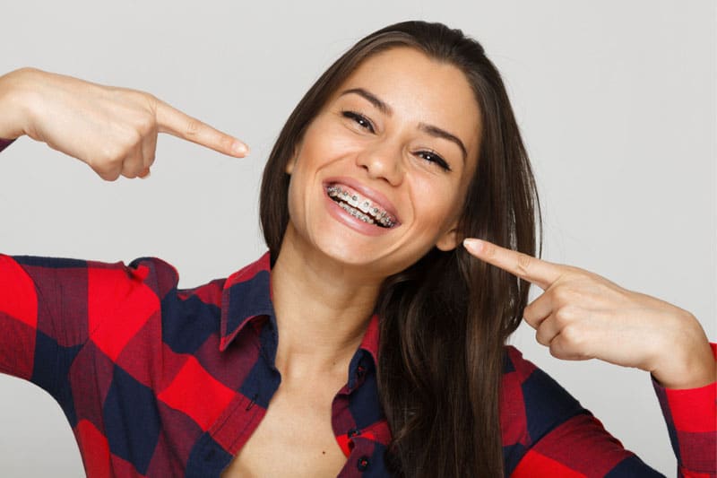 dark haired woman smiling and pointing at her teeth to show braces, orthodontist Melrose MA